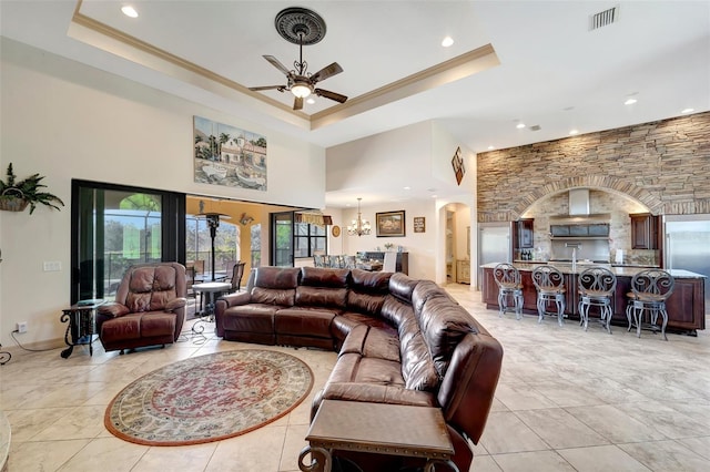 living room featuring a towering ceiling, a tray ceiling, and ceiling fan with notable chandelier