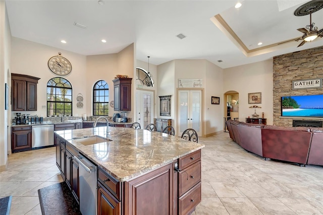 kitchen with a towering ceiling, dishwasher, sink, a kitchen island with sink, and light stone countertops