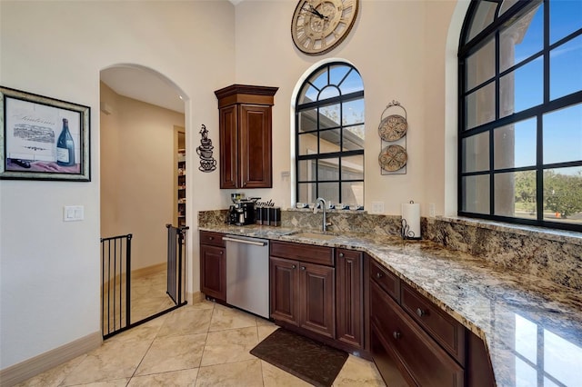 kitchen with light stone counters, sink, dark brown cabinets, and stainless steel dishwasher