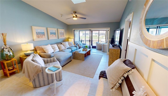 living room featuring ceiling fan, vaulted ceiling with skylight, and light tile patterned flooring