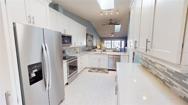 kitchen with lofted ceiling with skylight, tasteful backsplash, white cabinetry, light tile patterned floors, and stainless steel appliances