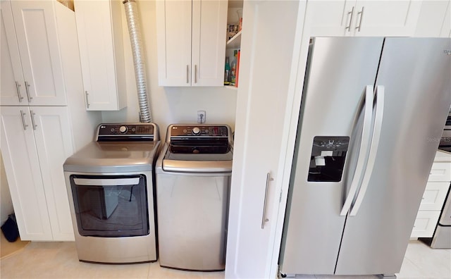 clothes washing area featuring cabinets, light tile patterned flooring, and washer and clothes dryer