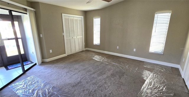 unfurnished bedroom with multiple windows, a closet, and dark colored carpet