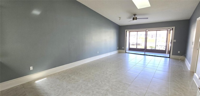 tiled empty room with vaulted ceiling with skylight and ceiling fan