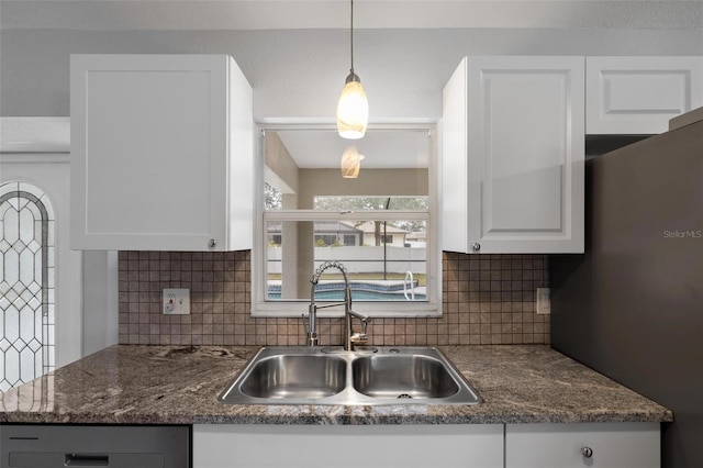 kitchen with pendant lighting, backsplash, freestanding refrigerator, white cabinetry, and a sink