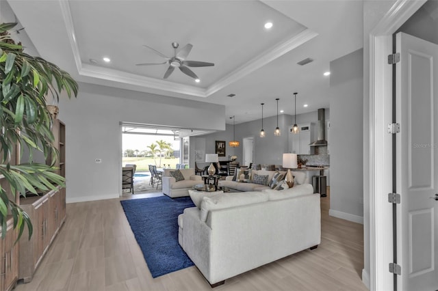 living room with a ceiling fan, baseboards, a tray ceiling, and crown molding