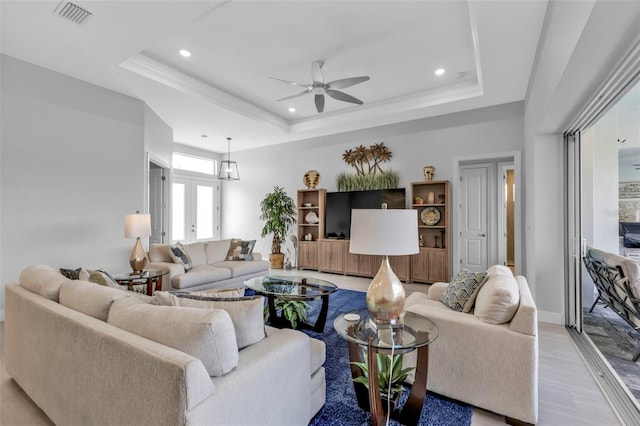 living area with light wood-style floors, a tray ceiling, visible vents, and a ceiling fan