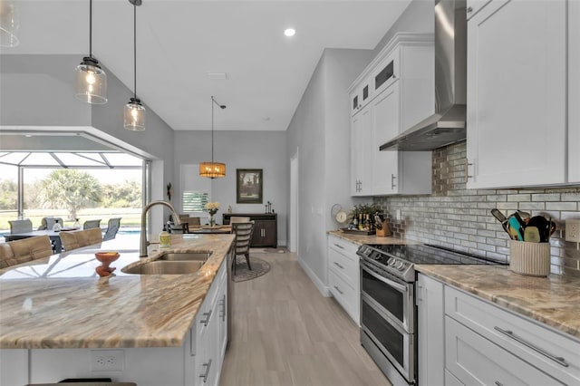 kitchen with range with two ovens, a sink, white cabinetry, wall chimney exhaust hood, and a center island with sink