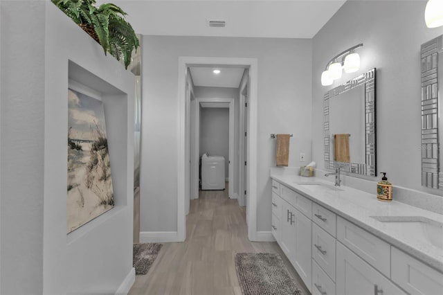 full bath with double vanity, wood finished floors, a sink, and baseboards