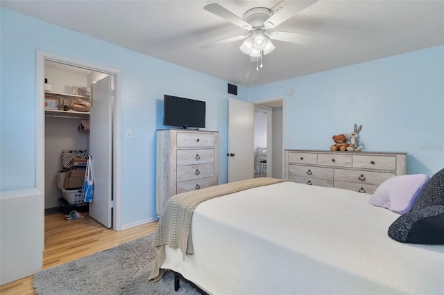 bedroom featuring ceiling fan, a textured ceiling, a spacious closet, a closet, and light wood-type flooring