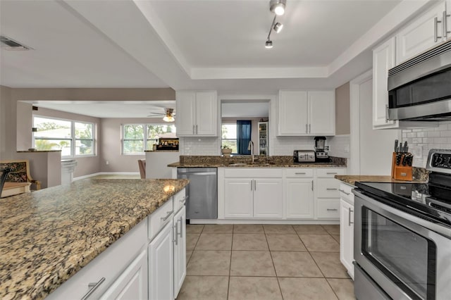 kitchen featuring sink, light tile patterned floors, appliances with stainless steel finishes, dark stone counters, and white cabinets