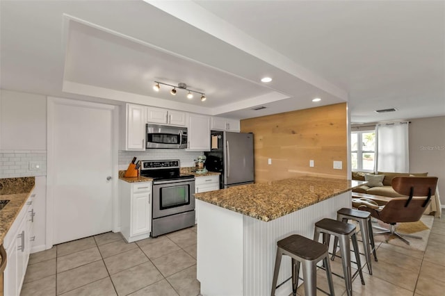 kitchen with a breakfast bar, appliances with stainless steel finishes, white cabinets, decorative backsplash, and a raised ceiling