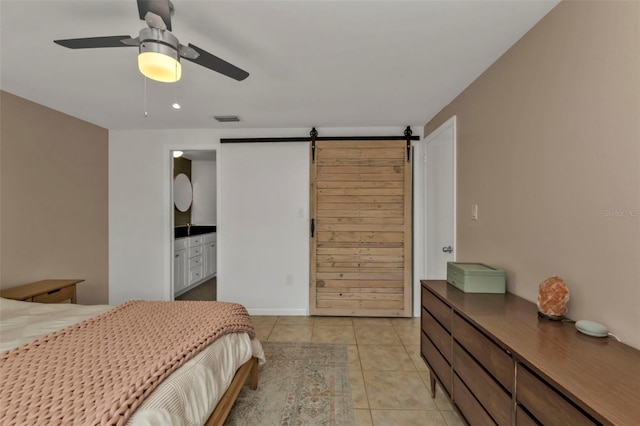 tiled bedroom featuring ceiling fan, a barn door, and ensuite bath