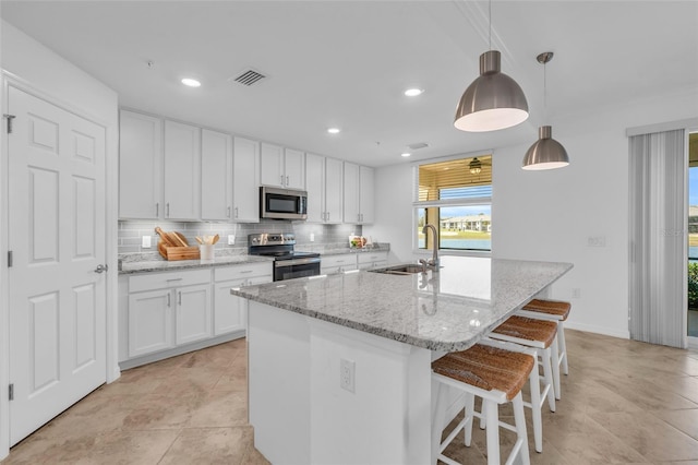 kitchen with pendant lighting, white cabinetry, a kitchen island with sink, stainless steel appliances, and light stone counters