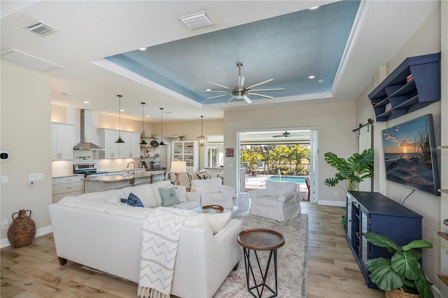 living room featuring crown molding, ceiling fan, a raised ceiling, and light hardwood / wood-style floors