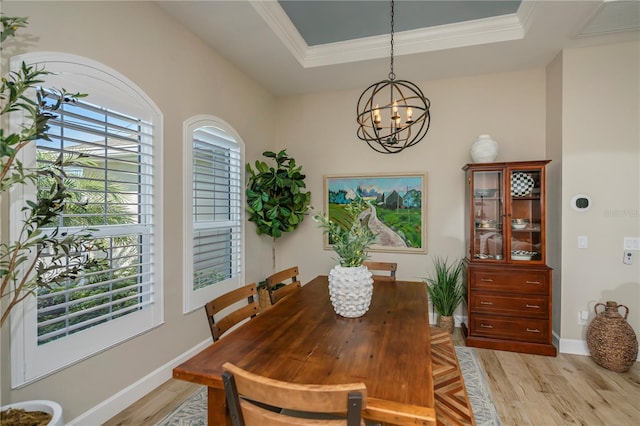 dining space with crown molding, a chandelier, light hardwood / wood-style floors, and a tray ceiling