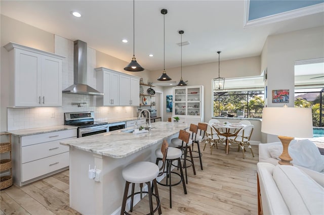 kitchen with pendant lighting, sink, stainless steel range with electric cooktop, white cabinets, and wall chimney exhaust hood