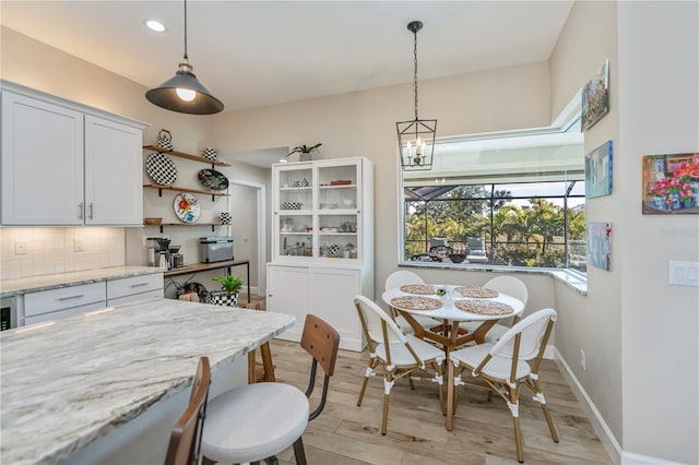 kitchen with light wood-type flooring, white cabinets, pendant lighting, light stone countertops, and backsplash