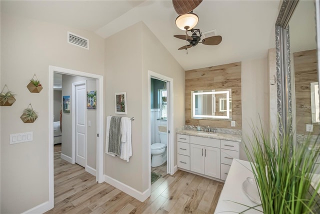 bathroom featuring lofted ceiling, toilet, vanity, hardwood / wood-style flooring, and ceiling fan