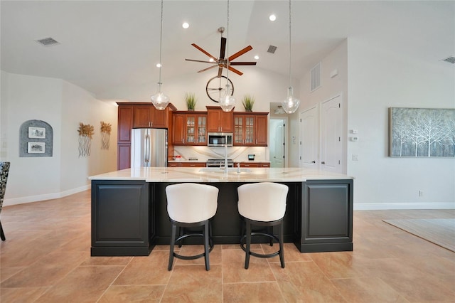 kitchen with light stone counters, high vaulted ceiling, a large island with sink, appliances with stainless steel finishes, and a kitchen breakfast bar