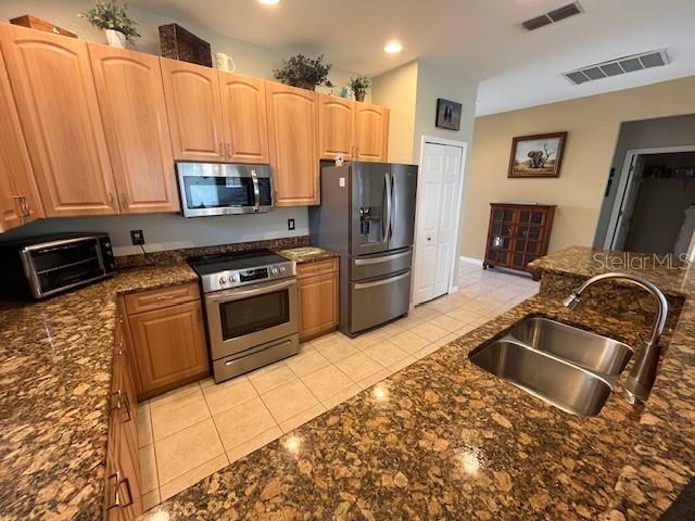 kitchen featuring stainless steel appliances, dark stone countertops, sink, and light tile patterned floors