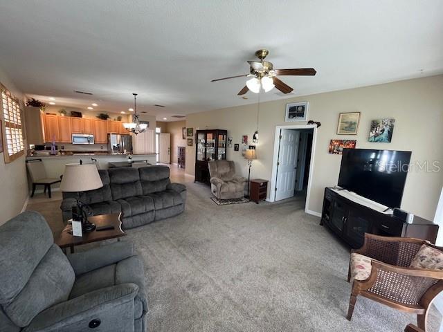 carpeted living room with ceiling fan with notable chandelier