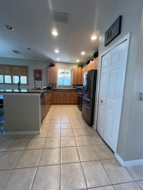 kitchen with light tile patterned floors, dishwasher, stove, black fridge, and kitchen peninsula