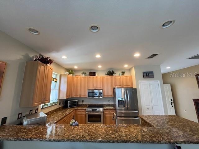 kitchen with dark stone counters, kitchen peninsula, and appliances with stainless steel finishes