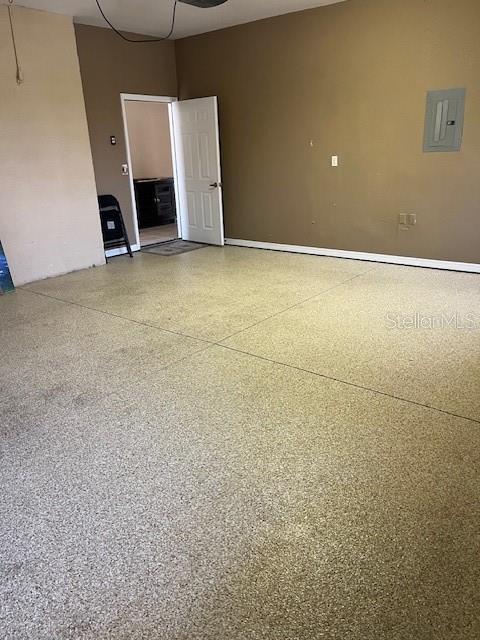 unfurnished room featuring baseboards, speckled floor, and electric panel