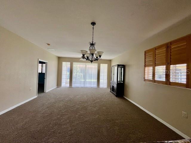 empty room featuring baseboards, a notable chandelier, and carpet