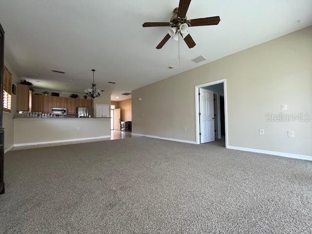 unfurnished living room featuring baseboards, carpet flooring, and ceiling fan with notable chandelier