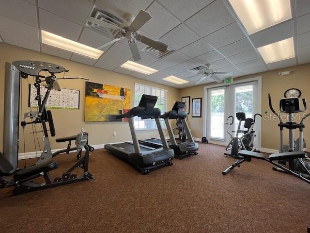 exercise room featuring a paneled ceiling, baseboards, a ceiling fan, and visible vents