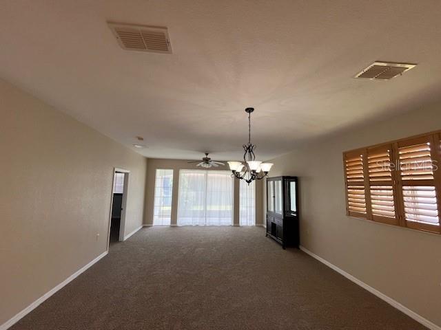 empty room with baseboards, visible vents, carpet, and ceiling fan with notable chandelier