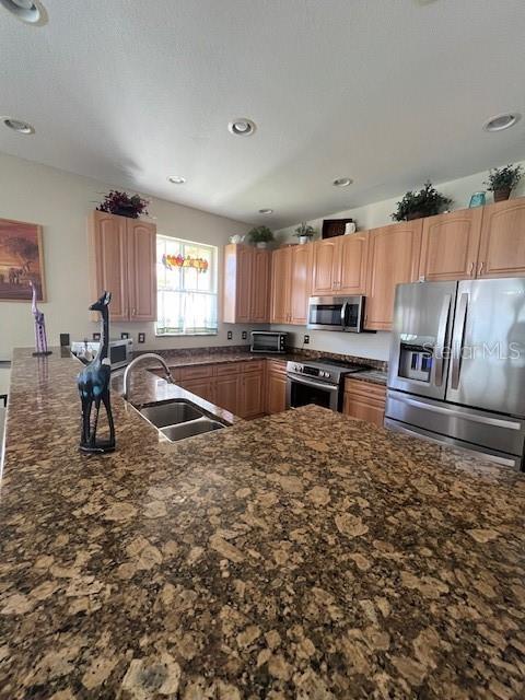 kitchen with a sink, dark stone countertops, a toaster, recessed lighting, and appliances with stainless steel finishes