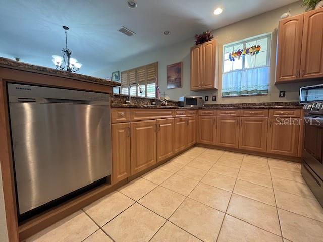 kitchen with stainless steel appliances, an inviting chandelier, dark stone countertops, and light tile patterned flooring