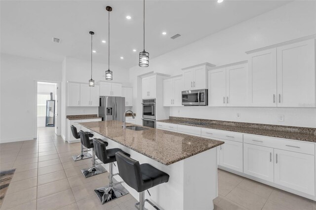 kitchen featuring a breakfast bar area, white cabinetry, decorative light fixtures, stainless steel appliances, and a kitchen island with sink