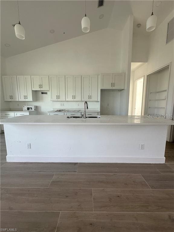 kitchen with an island with sink, hanging light fixtures, and white cabinets