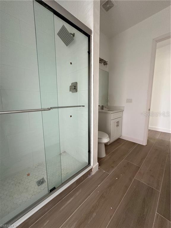 bathroom featuring vanity, a shower with door, and toilet