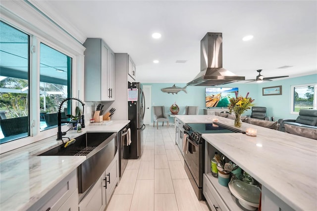 kitchen with island range hood, sink, stainless steel fridge, electric range, and light stone counters