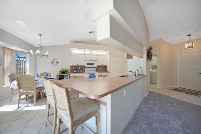 kitchen featuring a kitchen bar, pendant lighting, white appliances, and kitchen peninsula