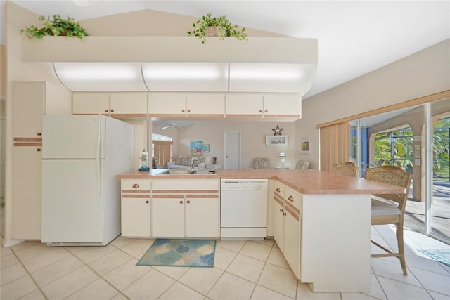 kitchen featuring sink, white appliances, a breakfast bar area, light tile patterned floors, and kitchen peninsula