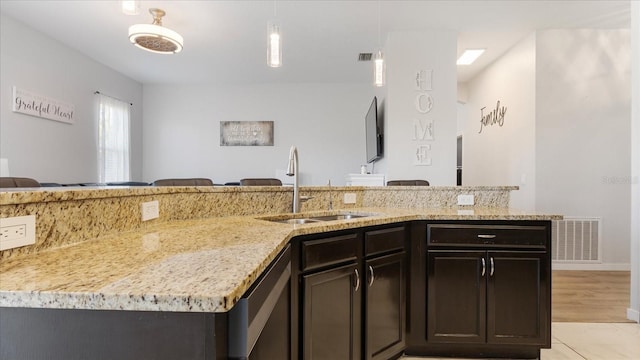 kitchen featuring sink, dishwasher, light stone countertops, hanging light fixtures, and dark brown cabinetry