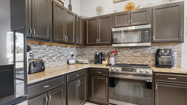 kitchen featuring decorative backsplash, stainless steel appliances, dark brown cabinetry, and light stone counters