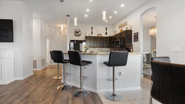 kitchen featuring light stone countertops, sink, dark brown cabinets, a breakfast bar area, and decorative backsplash