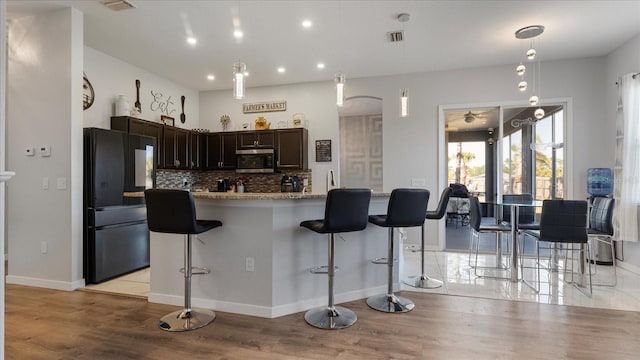 kitchen with light hardwood / wood-style flooring, a kitchen breakfast bar, black refrigerator, dark brown cabinetry, and decorative backsplash