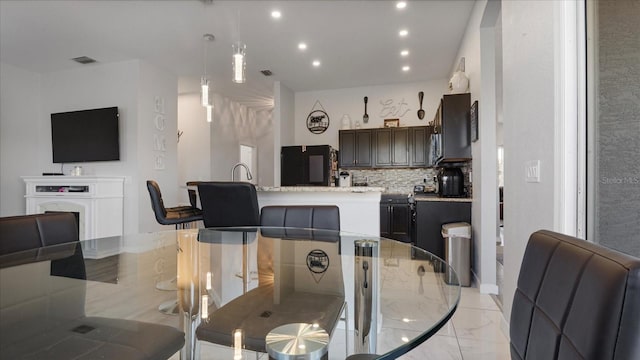 kitchen featuring backsplash, fridge, hanging light fixtures, dark brown cabinets, and a kitchen island with sink