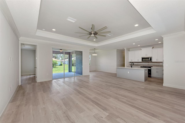 unfurnished living room featuring a raised ceiling, crown molding, light wood-type flooring, and ceiling fan