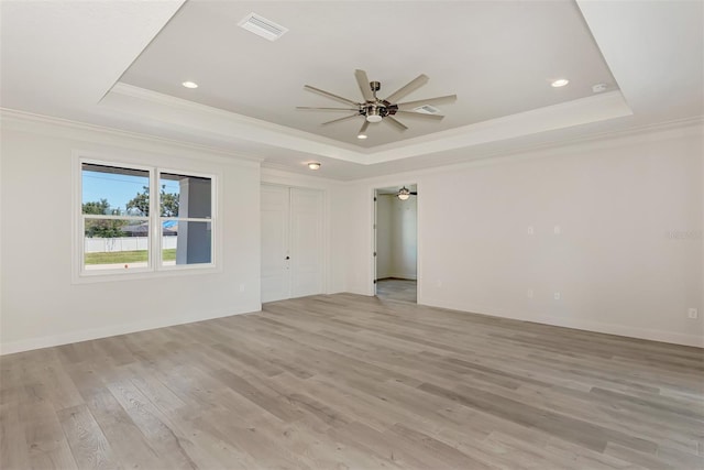 empty room featuring crown molding, a tray ceiling, and light wood-type flooring