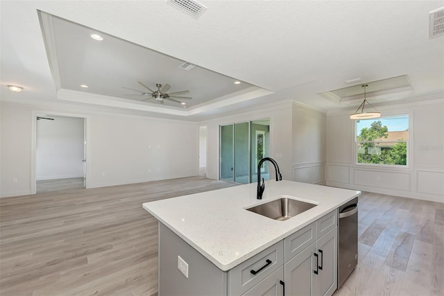 kitchen featuring a raised ceiling, an island with sink, hanging light fixtures, and sink