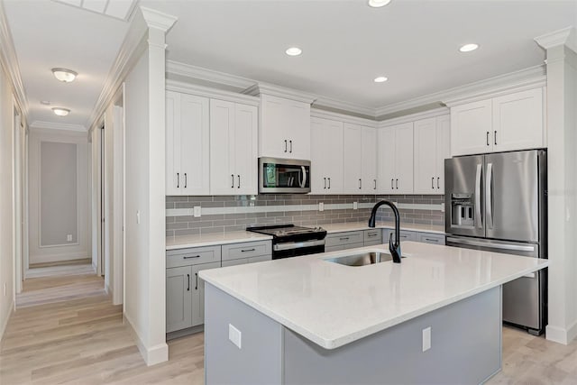 kitchen with appliances with stainless steel finishes, sink, white cabinets, a kitchen island with sink, and light hardwood / wood-style floors